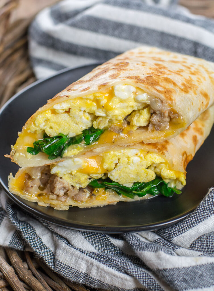 Breakfast burrito cut in half showing eggs, potatoes, peppers, and melted cheese.